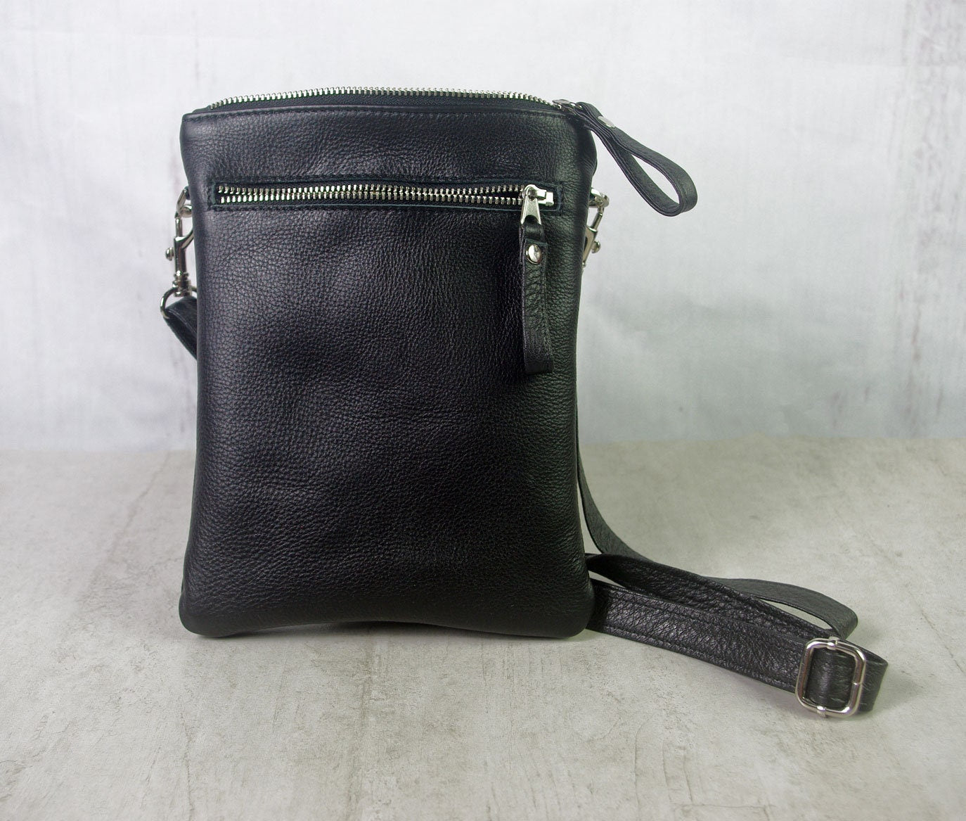 Black leather crossbody bag on a light gray surface with a white background
