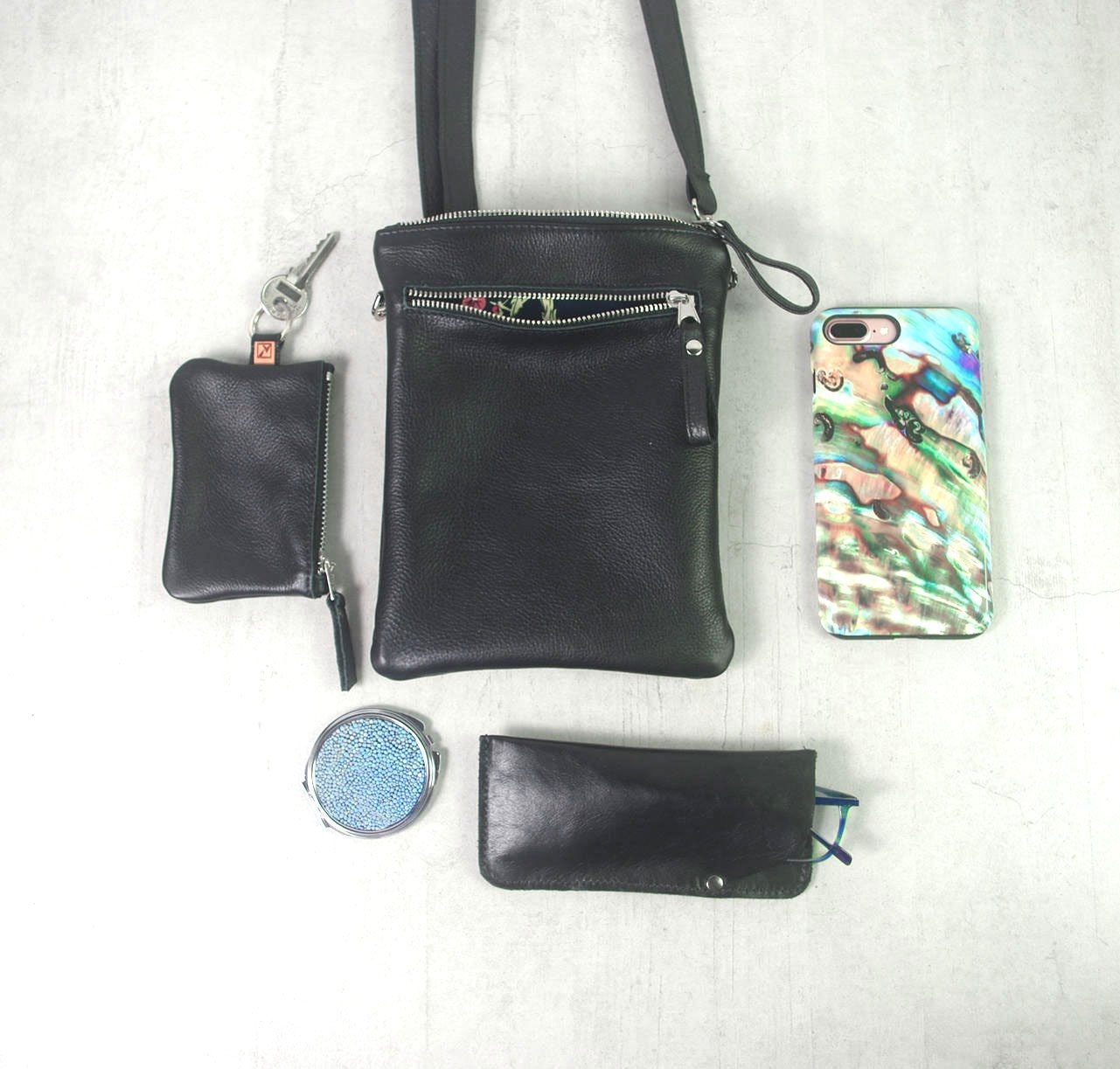 Black handbag with smaller black pouches, a phone case, and a compact mirror on a white background