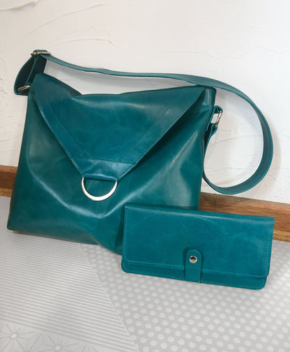 Teal leather handbag has flap and magnet closure with matching wallet on a textured surface