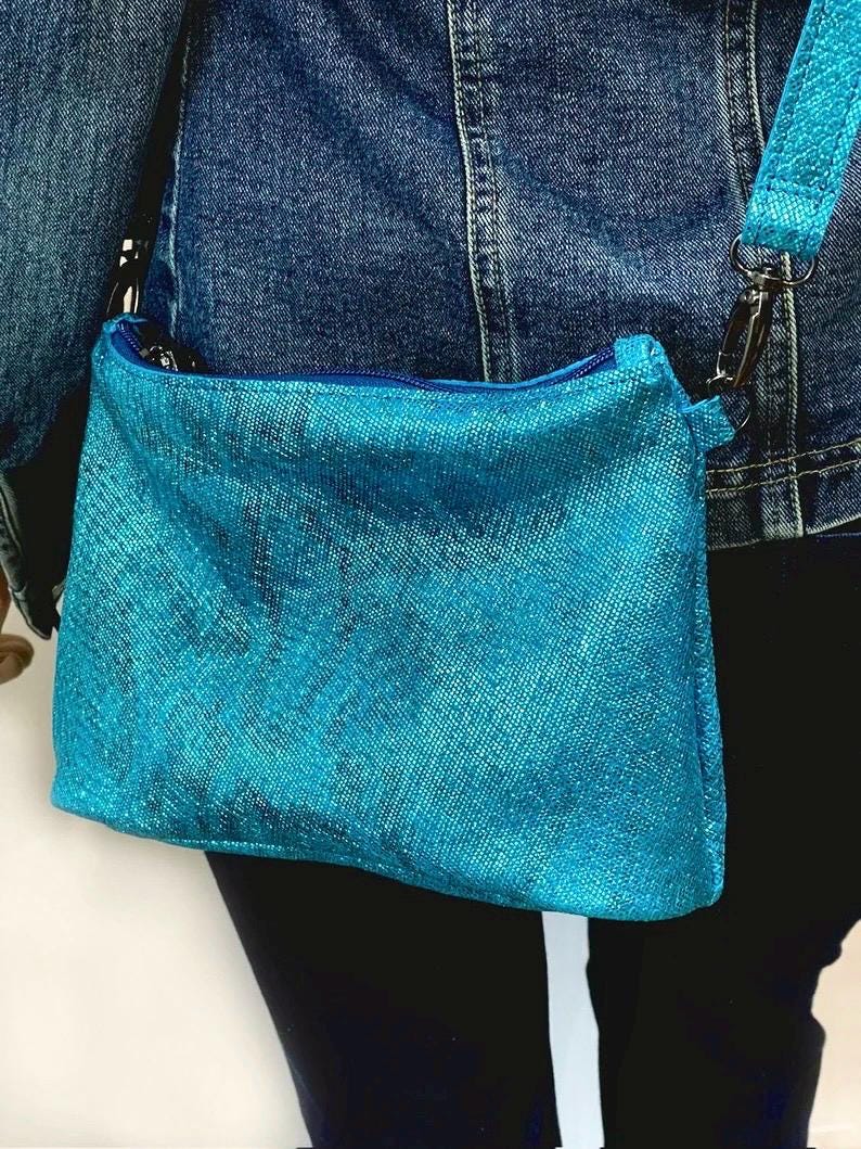 printed texture teal blue handbag worn over a person's shoulder against a neutral background