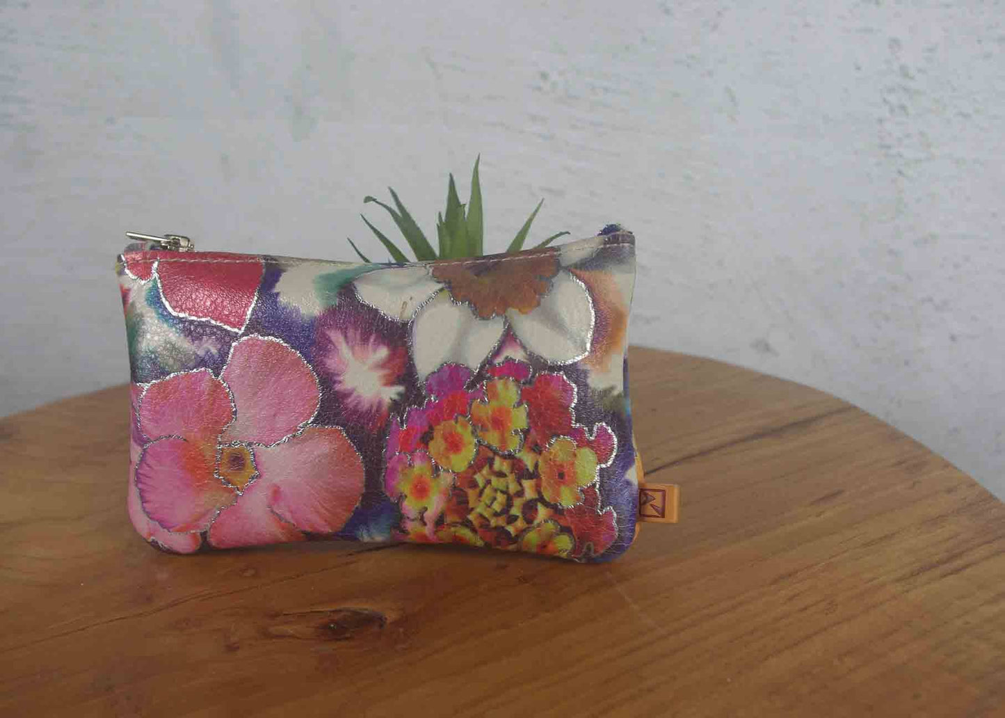 Floral-patterned pouch on a wooden surface with a white wall background