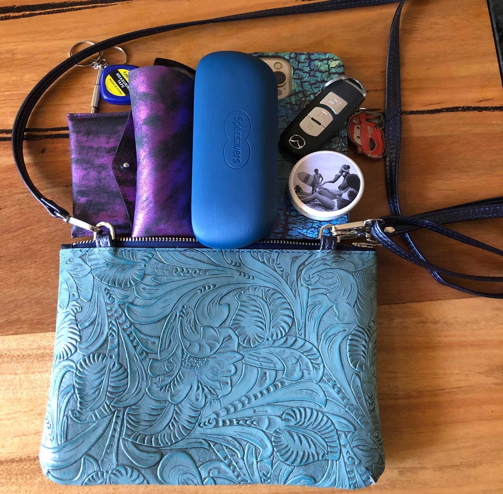 Blue patterned pouch with sunglasses, phone, and other items showing how many items fit into this small purse.