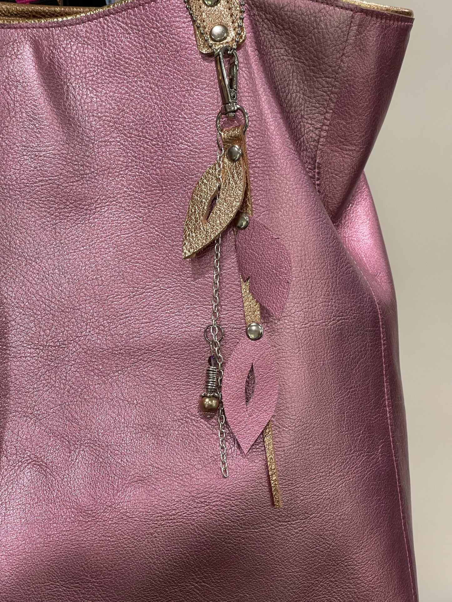 Close-up of a soft pink leather bag with leaf-shaped charm keychain details.