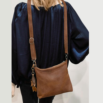 mid Brown leather bag with strap over shoulder on a plain background
