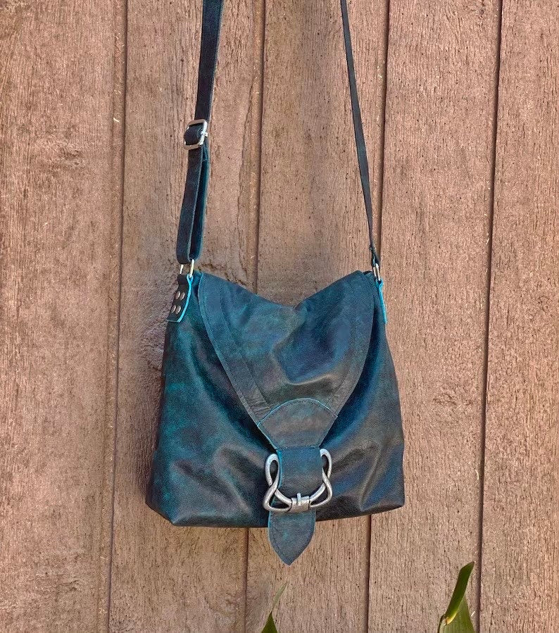 vintage teal leather handbag has V flap with celtic buckle with a strap on a wooden surface