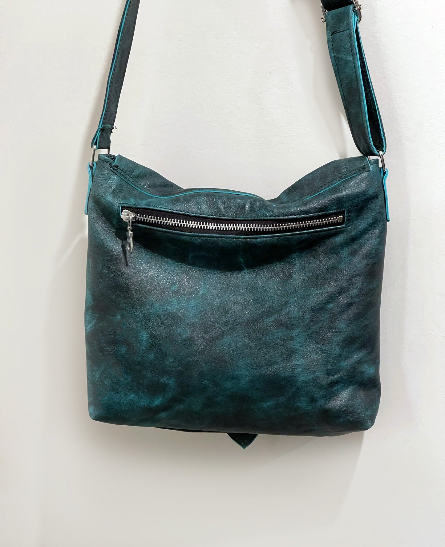 Teal leather handbag with a visible silver zipper on a white background